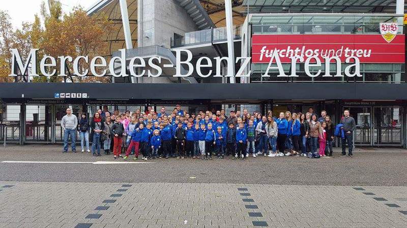 Eine Gruppe von Menschen versammelt sich vor der Mercedes-Benz Arena für ein gemeinsames Foto.