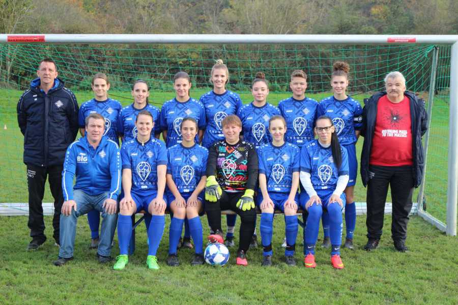 Eine Gruppe von Spielerinnen im Fußballtrikot posiert fröhlich für ein Foto.