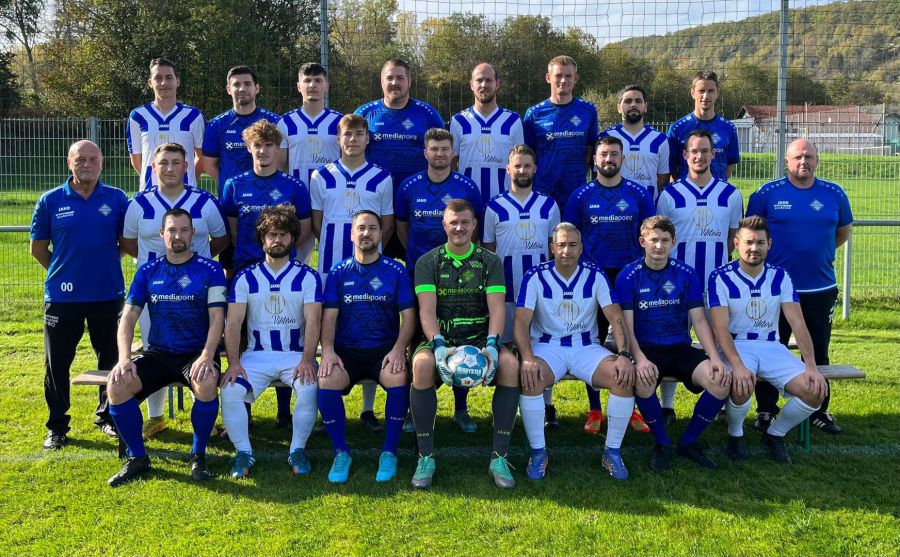 Teamfoto einer Fußballmannschaft, die Spieler stehen auf dem Feld und posieren freundlich für die Kamera.